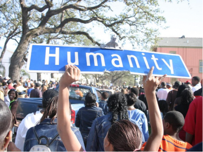 A person holding up a street sign titled "humanity" while marching