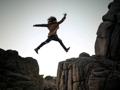 woman leaping over space between rocks