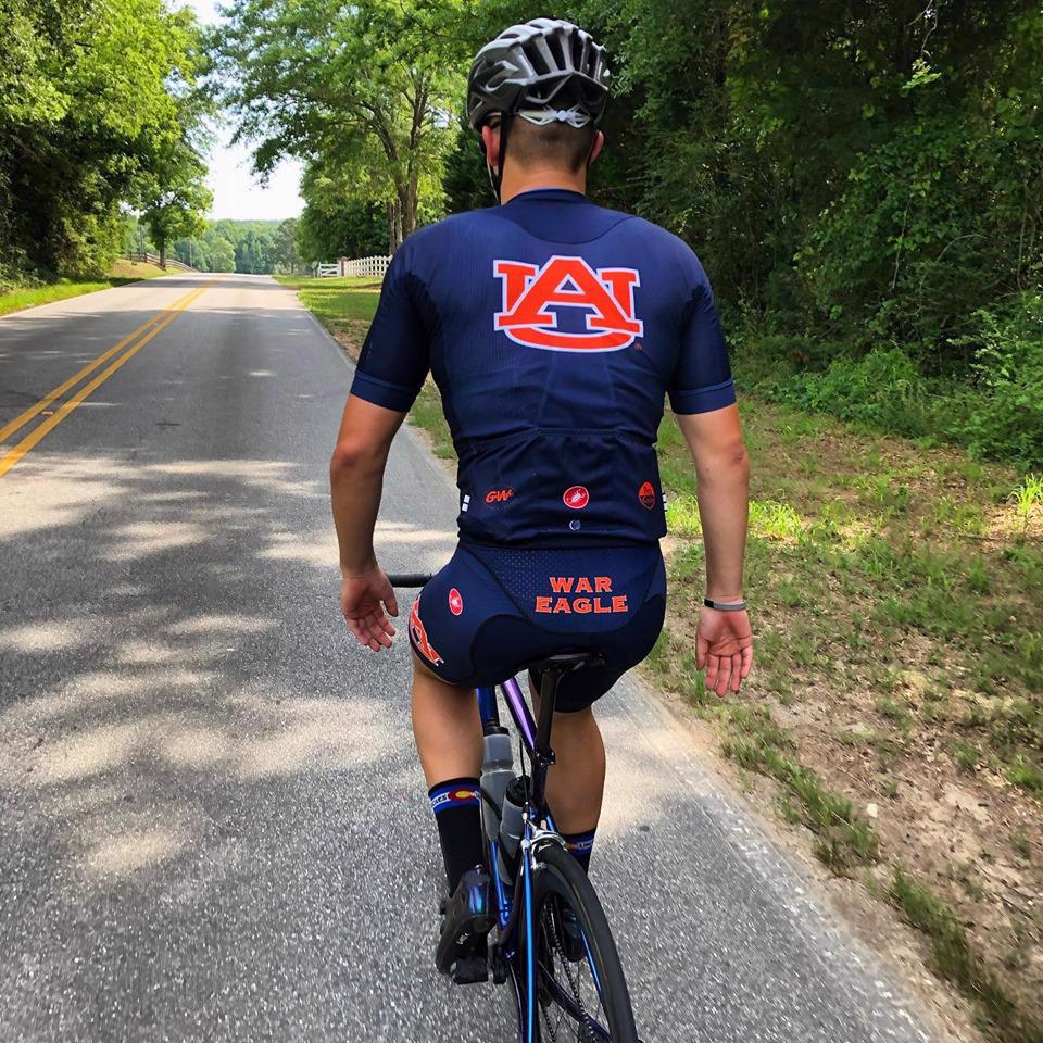 Photo of person riding a bicycle with an Auburn biking uniform on.