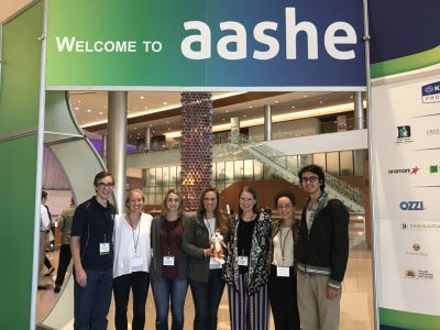 Photo of people standing in front of a sign reading “Welcome to AASHE”