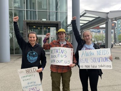 Photo of individuals with their fists raised and holding signs protesting fossil fuels