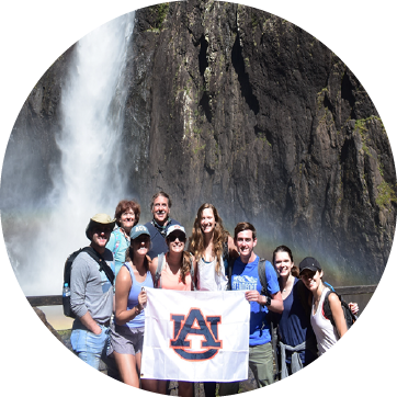 Auburn students in Australia holding a Auburn flag in front of a waterfall
