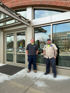 Two facilities management employees standing with the LEED Gold plaque