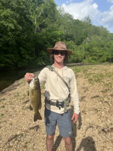 Young man standing near a river holding a smallmouth bass he just caught fishing
