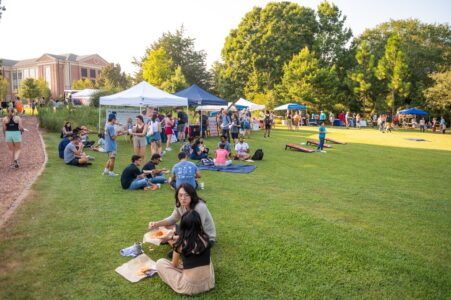 A lively college event with people, tents, and games on a sunny lawn.