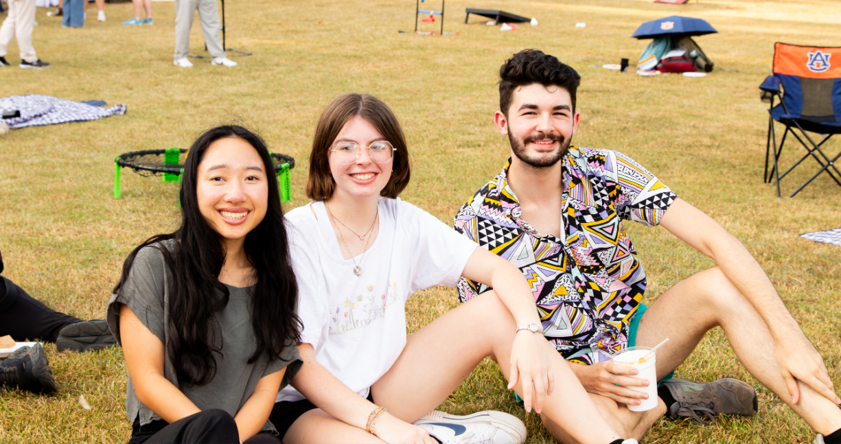 Three people seating in the ground and smiling to the camera.
