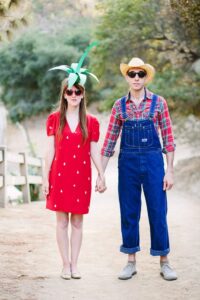 A couple holding hands dressed in a strawberry and farmer costume