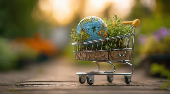 Small globe and plants inside miniature shopping cart promoting environmental protection, sustainable shopping, and Earth Day