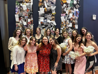 a photo of 14 students in front of a wall of art