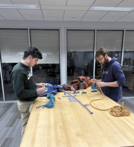 two men standing at a table making belts out of climbing rope