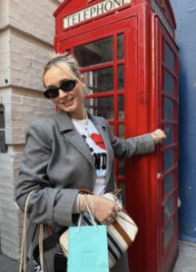 girl with an "I heart London" shirt outside of a red vintage-style telephone booth