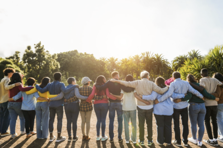 16 people linked together through a hug in a line facing the sunset